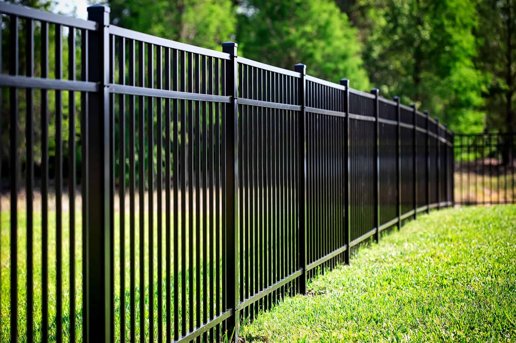 Black aluminum flat-top fence with pyramid post caps along a backyard lawn